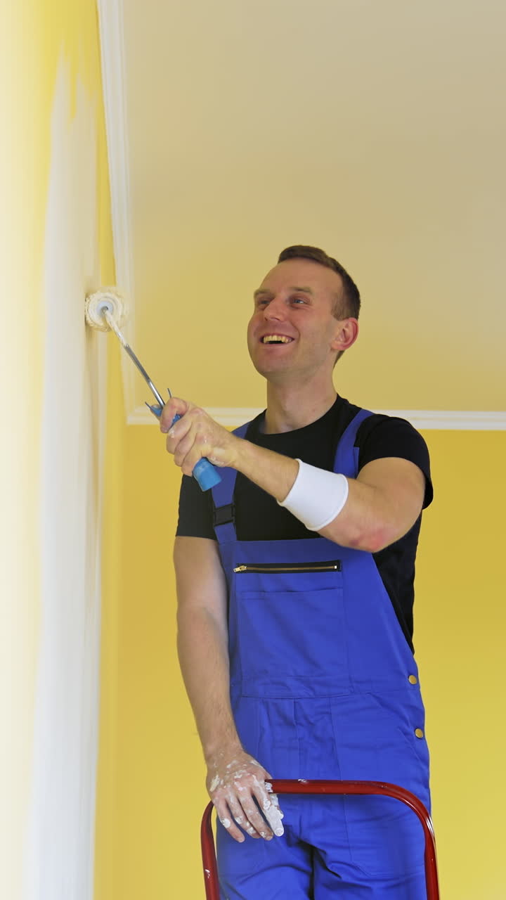 Attractive handsome repairman doing renovation the wall. Painter man at work painting an orange wall with a roller. Vertical video