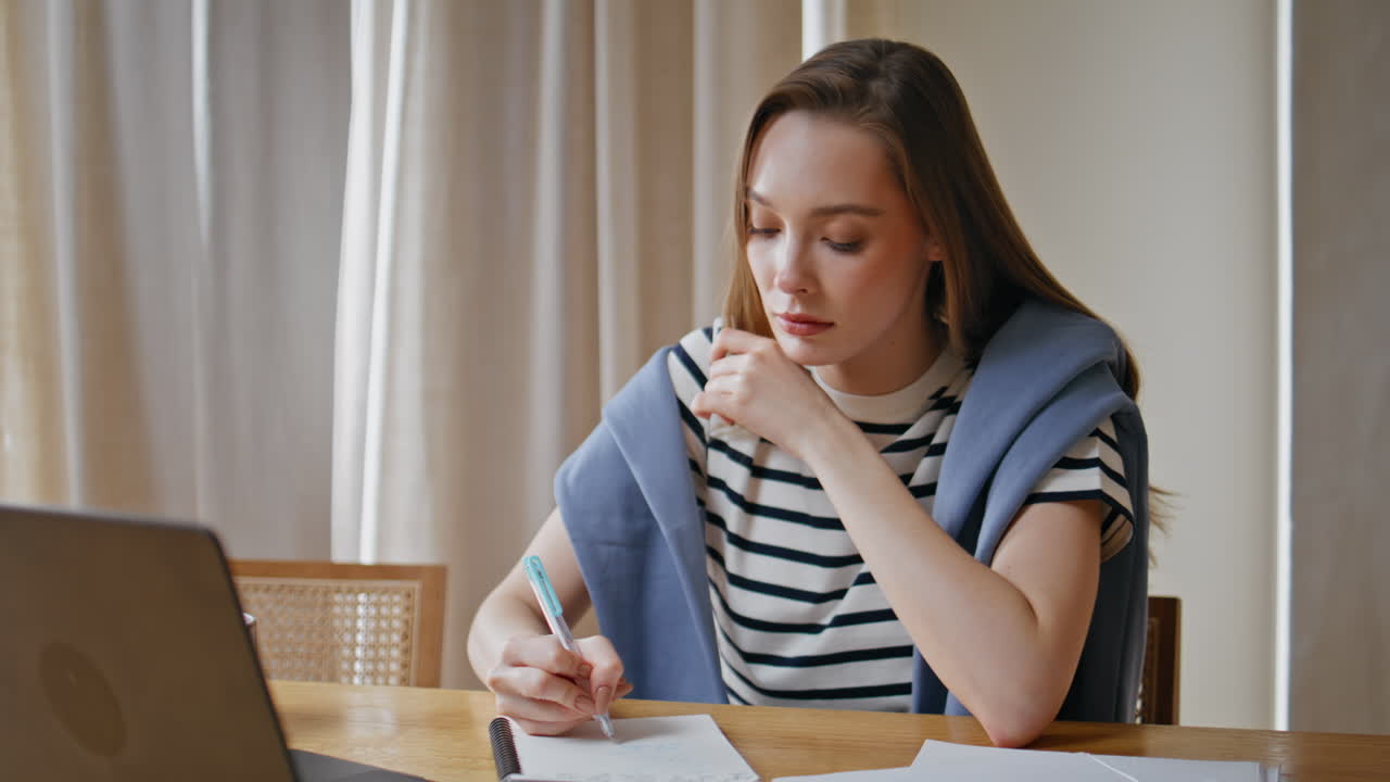 Freelance worker writing notes looking laptop screen in apartment closeup
