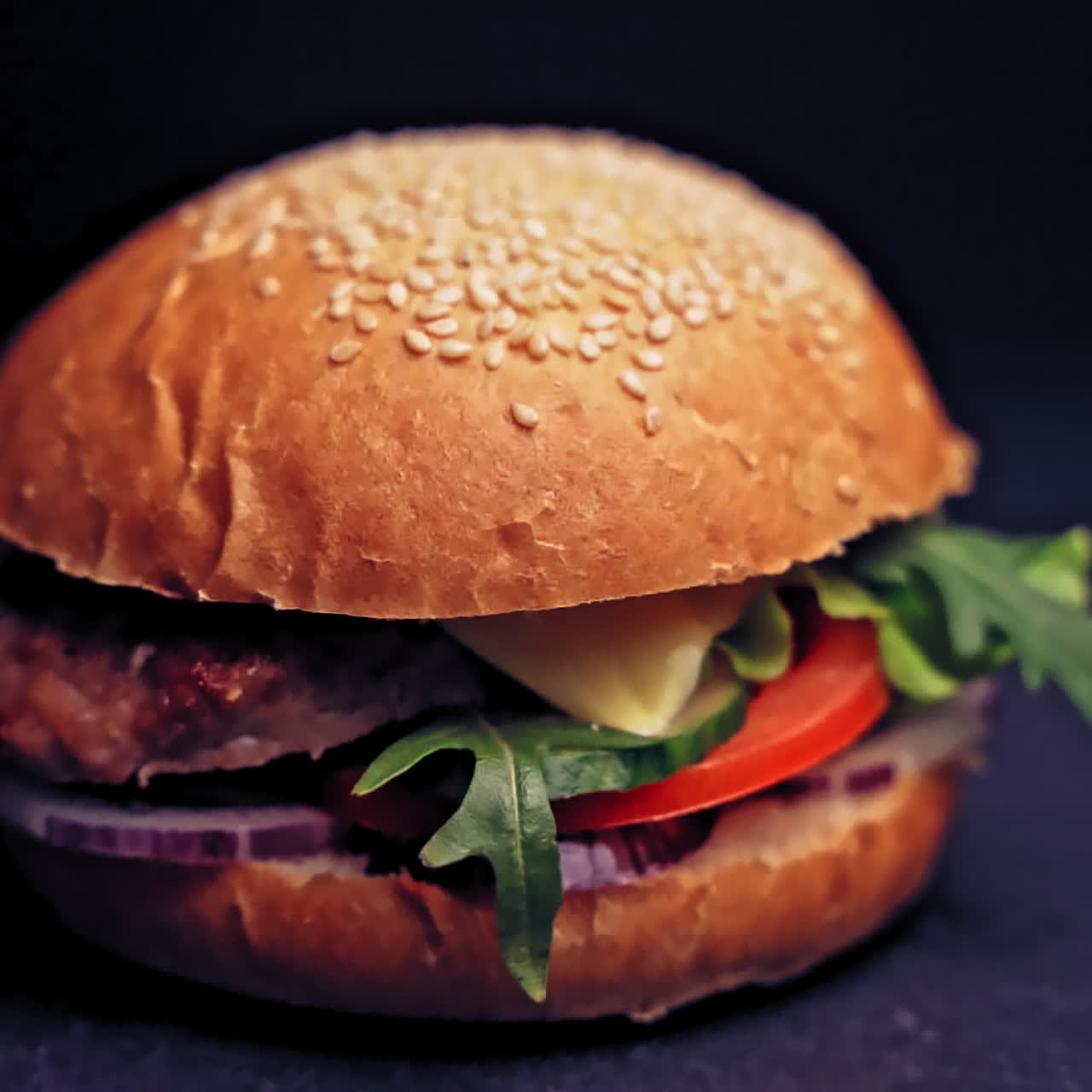 Great Burger with beef cutlet, tomatoes, mushrooms and cucumbers with melted cheese rotates on a wooden Board on a dark background.