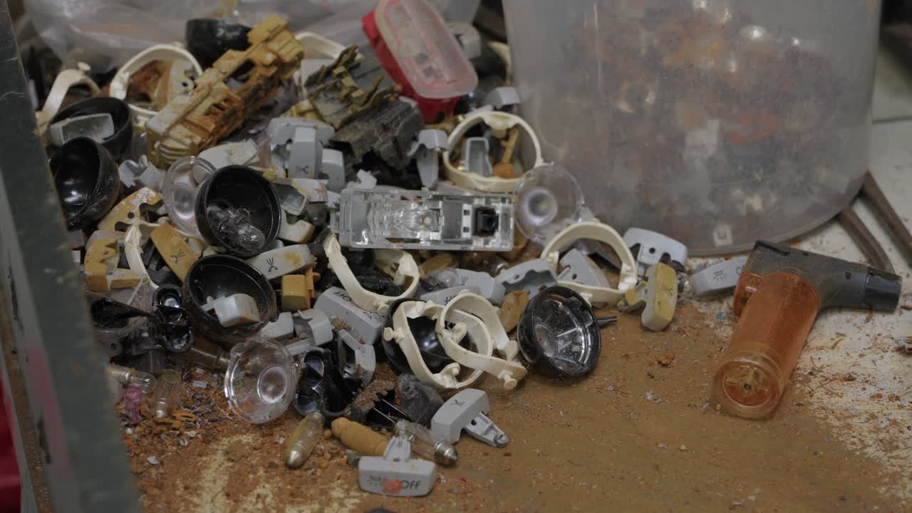 Cumulo di componenti in plastica e metallo smontati sparsi in un contenitore sporco.