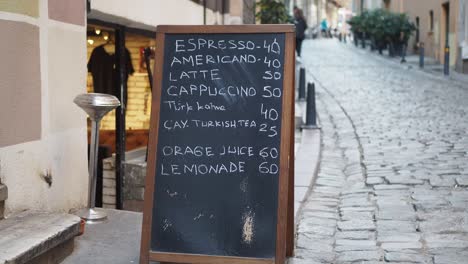 a cafe sign with drink prices on a cobblestone street