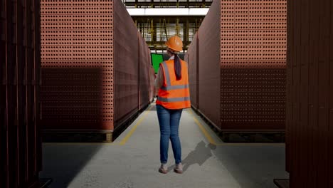 full body back view of asian female engineer with safety helmet working on a green screen tablet and looking around with red brick packed in stacks are stored