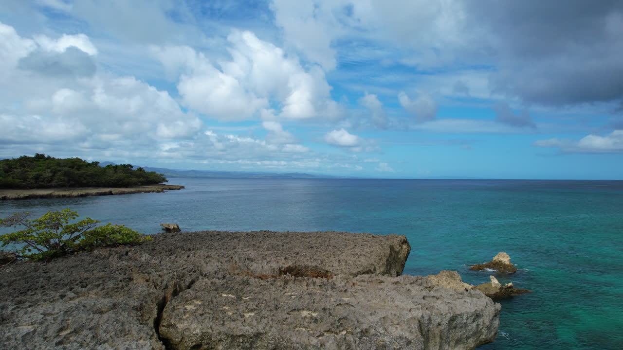 Ripresa aerea in avvicinamento della bandiera della Repubblica Dominicana su un masso e il Mar dei Caraibi sullo sfondo.