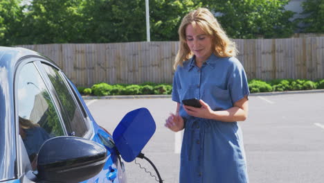mujer cargando un coche eléctrico con cable usando una aplicación en el teléfono para monitorear el nivel de la batería