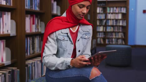 Una-Estudiante-Asiática-Con-Un-Hijab-Rojo-Estudiando-En-Una-Biblioteca-Y-Usando-Una-Tableta