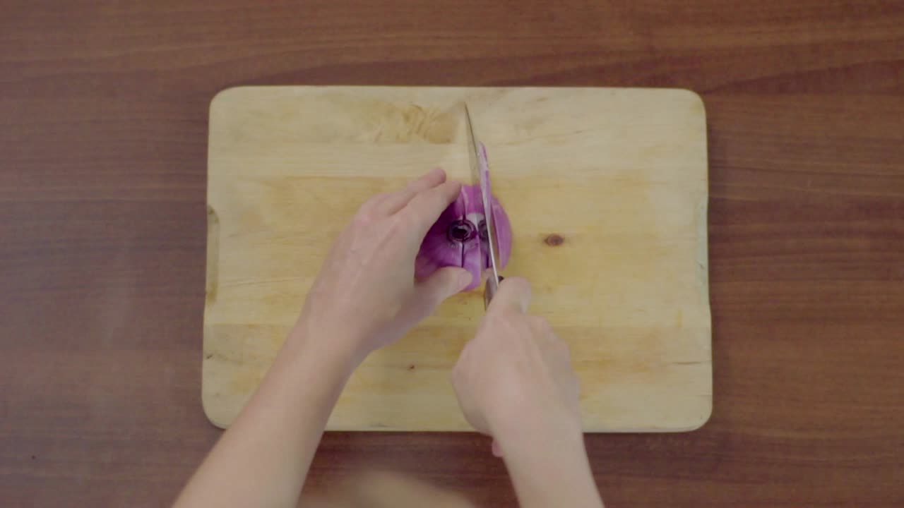 Top Down View of Hands Slicing a Red Onion on a Wooden Cutting Board