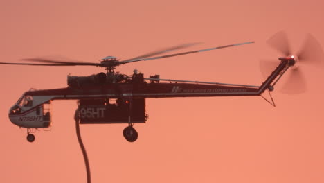 in glowing red sky an elvis water bombing helicopter descends to refill tanks