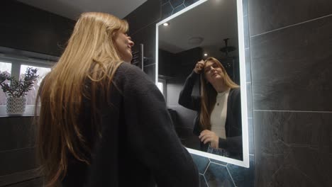 female model walking up to backlit bathroom mirror turning lights on with hand then turning lights off with hand