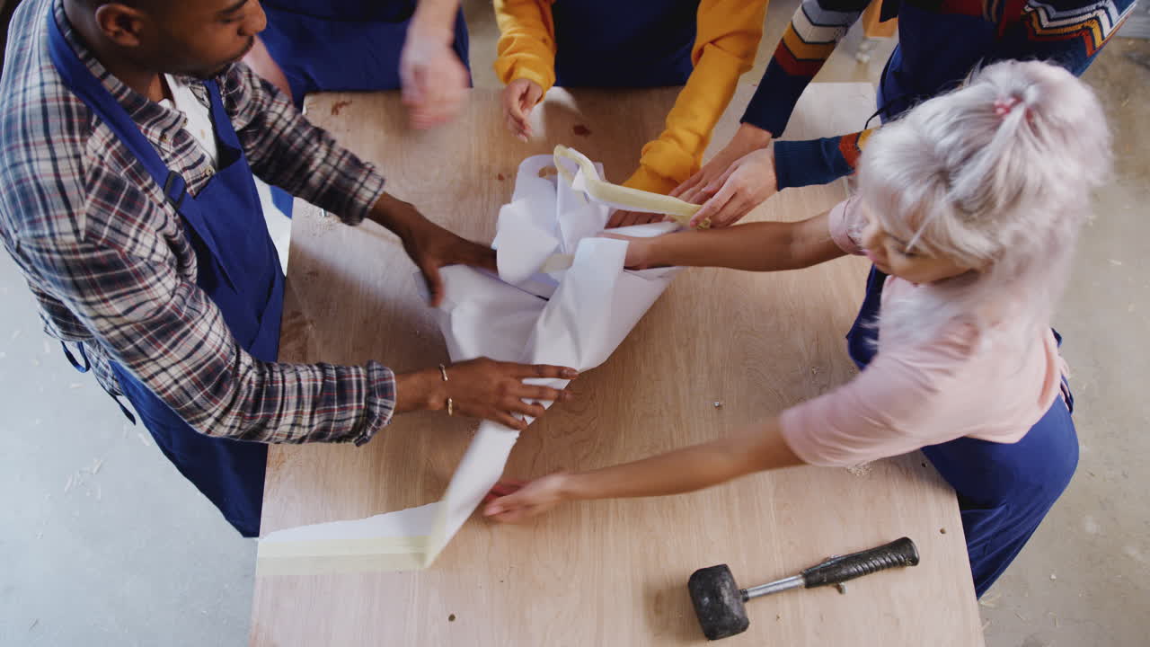 Overhead Shot Of Multi-Cultural Team In Workshop Tidying Workbench