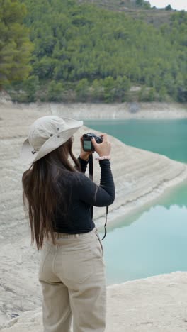 woman photographing a turquoise lake with low water level