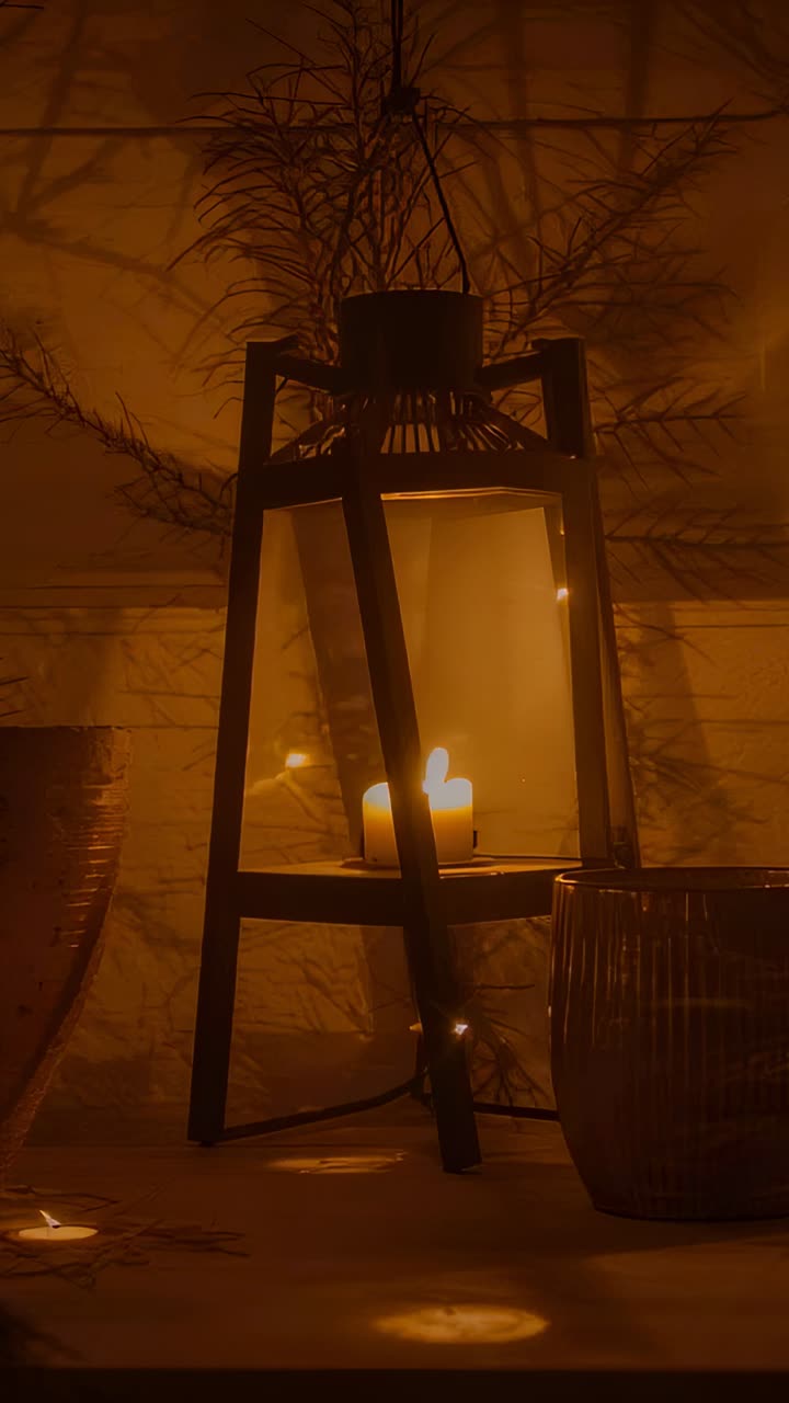 Vertical video: Flickering candle flame in lantern casting light on shelf, plant shadows moving