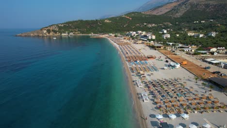gran playa con arena blanca, bares de playa y sombrillas en la costa mediterránea con agua de mar azul cristalino en himara