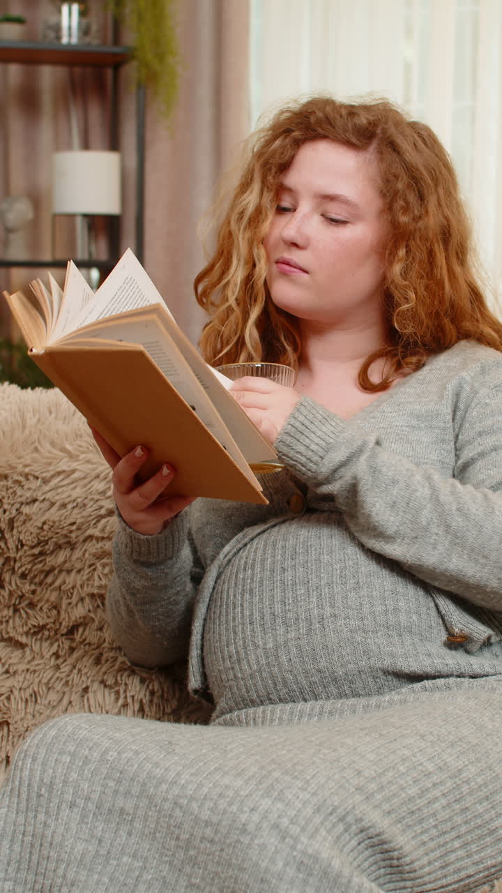 Pregnant young woman drinking orange juice while reading pregnancy book at home calm relaxed mood