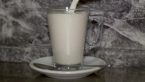 Filling-a-glass-of-milk-with-handle,-using-cool-metal-pitcher,-silver-spoon-in-front