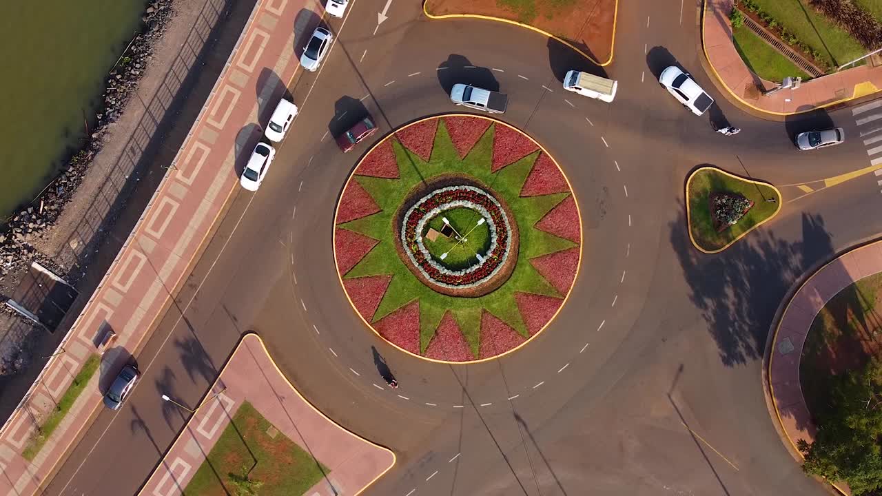 Cars driving in a flamboyant roundabout from a bird's eye view