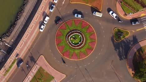 Cars driving in a flamboyant roundabout from a bird&#039;s eye view