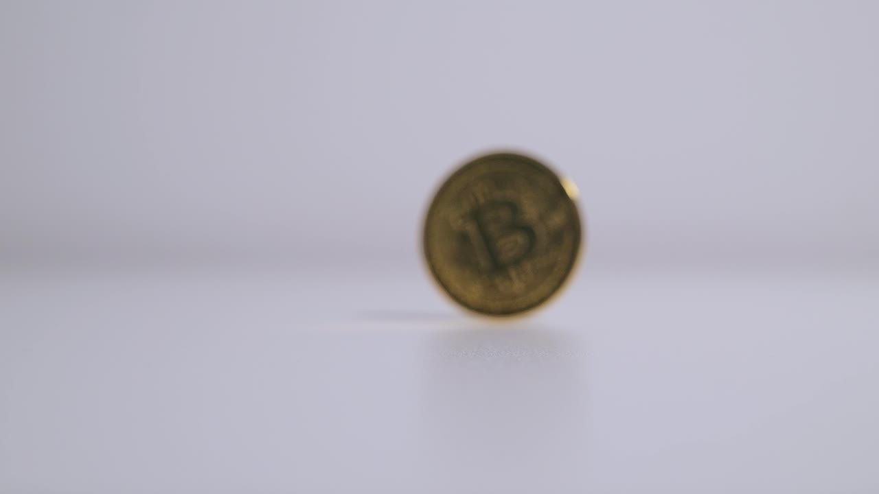 Gold Bitcoin coin is spun in slow motion on a white surface, digital finance