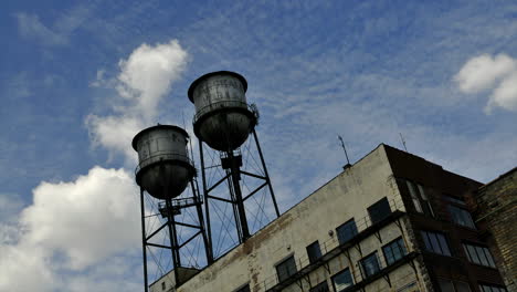 Timelapse-of-clouds-blowing-above-a-building-with-two-water-towers-on-top