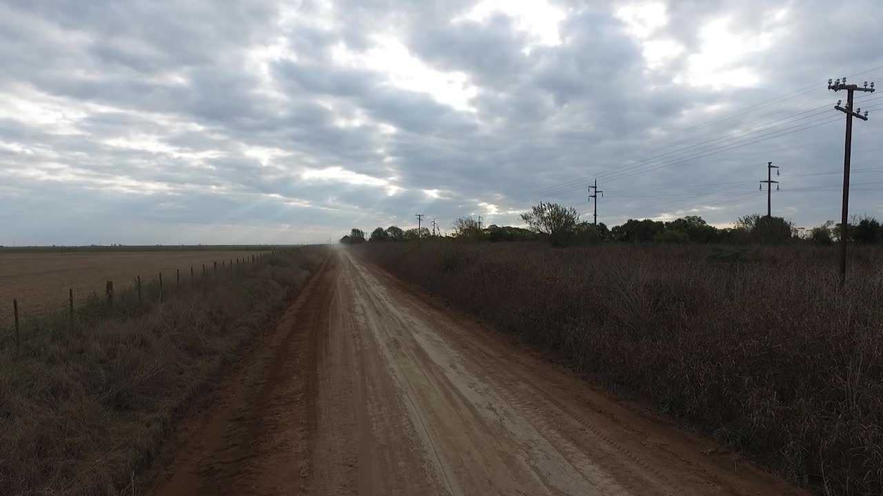 Drone shot of a dust pick up cloud moving away down a dirt road in the countryside