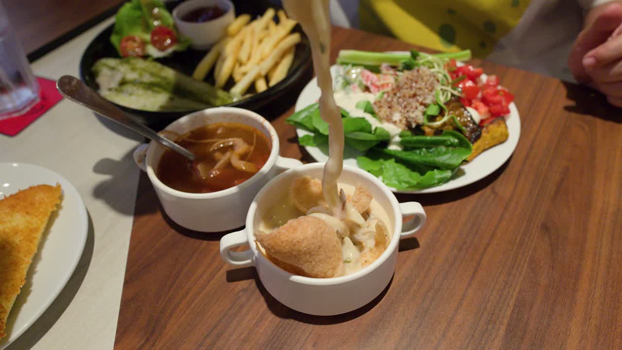 Hand lifts creamy pasta from soup bowl beside salad, fries, and bread in restaurant