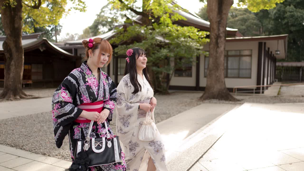 Due amici in kimono tradizionali camminano e parlano attraverso il cortile soleggiato di un santuario shintoista.