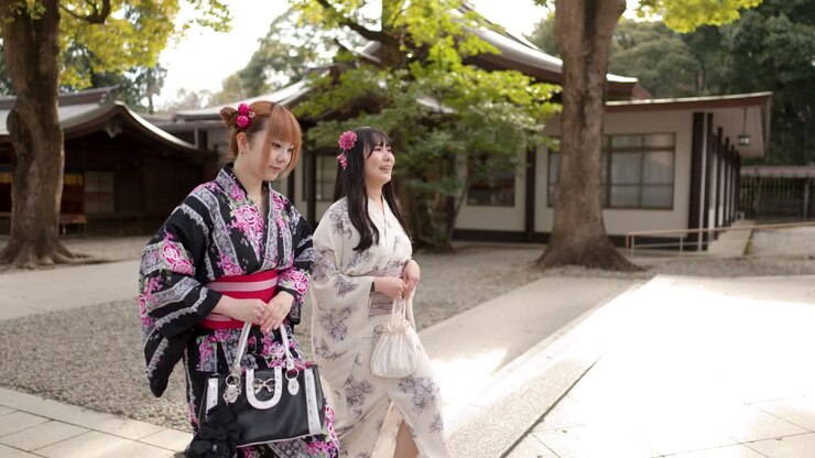 Due amici in kimono tradizionali camminano e parlano attraverso il cortile soleggiato di un santuario shintoista.