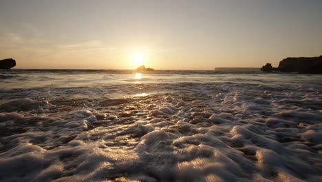 close-up of foamy ocean waves gently rolling onto the shore as the sun sets in algarve, portugal