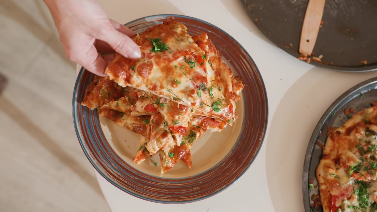 Fågelperspektiv av en hand som lyfter en bit nybakad lasagne från en keramiktallrik bredvid en stekpanna, vilket avslöjar lager av pastaplattor, smakrik köttfyllning, tjock tomatsås och smält gyllene ost