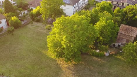 Drohnenansicht-Eines-Feldes-In-Der-Nähe-Von-Häusern-Während-Eines-Sonnenuntergangs-In-Italien,-Schöne-Sonnenstrahlen