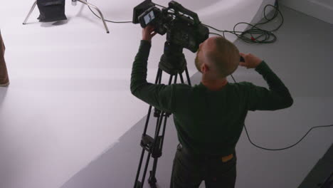 Overhead-Shot-Of-Male-Film-Camera-Operator-Focusing-Camera-Using-Monitor-Shooting-Movie-Or-Video-In-Studio