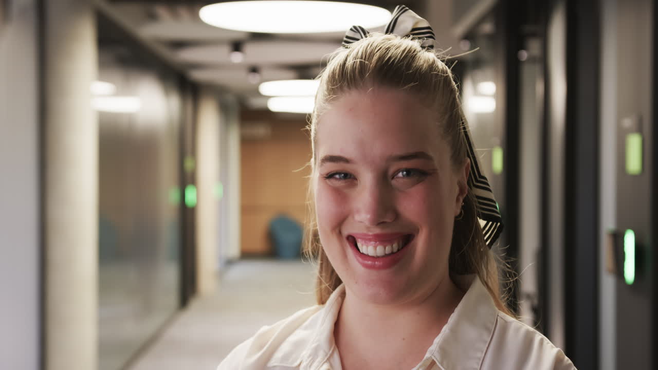 Smiling businesswoman standing in office hallway, looking confident and professional