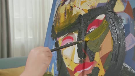 close up of a hand's girl holding paintbrush and painting a girl's face on the canvas