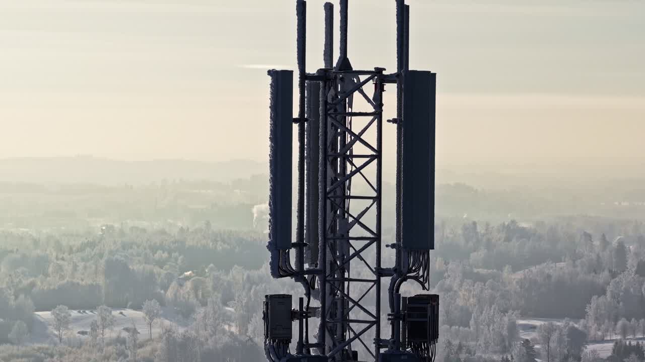 Frosty telecom cell tower with antenna panels rising above a misty winter landscape at sunrise, soft haze and copy space for technology or connectivity concepts