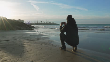 Man-takes-photo-of-sunset-golden-hour,-wide-beautiful-beach-with-waves-low-tide