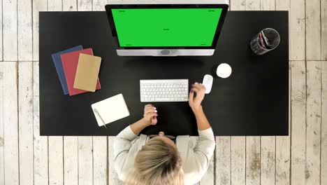 woman putting glasses on while using computer. green screen mock-up display