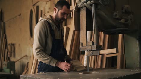 carpenter shop. a nice worker cuts a ribbed shape from a wooden block using an electric saw machine. evaluates the work, holding the product in hands