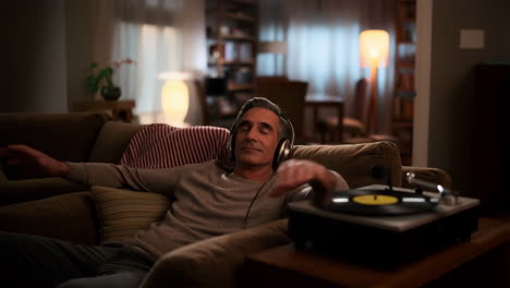 man relaxing on a couch listening to vinyl music with headphones