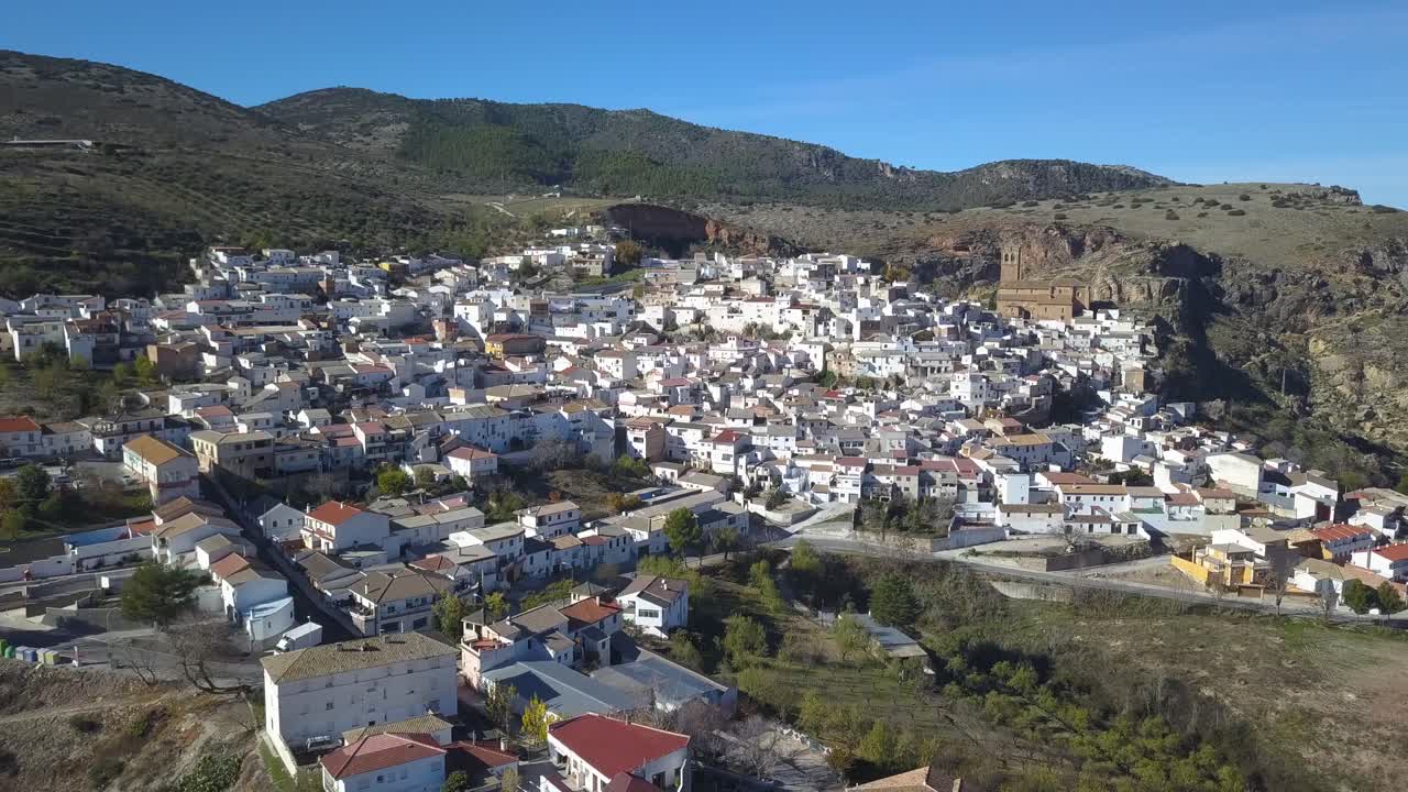 Vista aérea de un pueblo blanco español tradicional en las montañas con una iglesia grande.