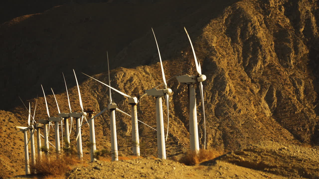 Steady shiot of miniaturised looking wind turbines rotating at a wind farm with huge mountain in the background near Palm Springs in the Mojave Desert, California, USA
