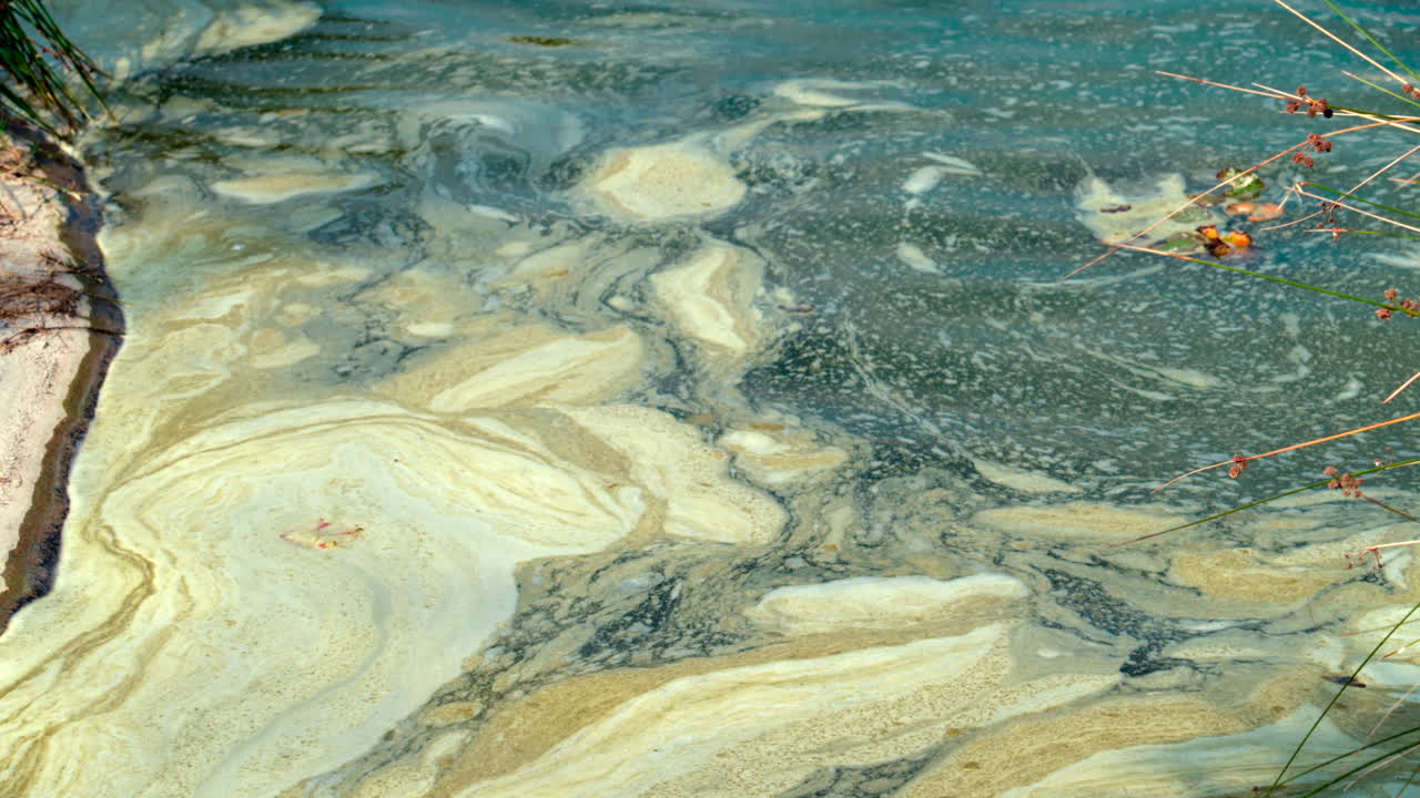Close up of dirty water with swirling yellowish foam patterns