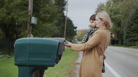 A-woman-with-a-child-in-her-arms-picks-up-a-letter-from-a-street-mailbox