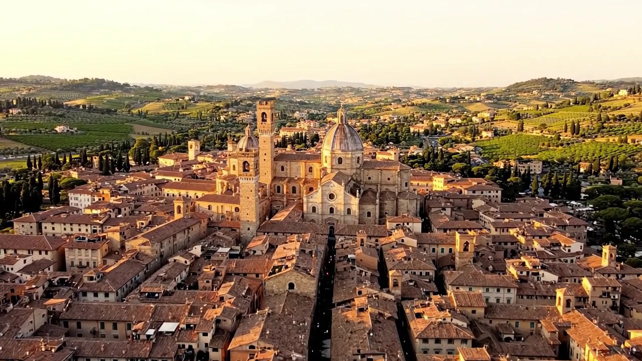 Veduta aerea di un'incantevole città storica circondata da lussureggianti colline verdi al tramonto, che mostra una splendida architettura e paesaggi sereni