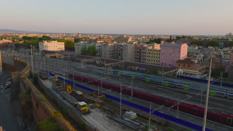 Slide-and-pan-footage-of-modern-high-speed-train-and-commuter-unit-leaving-station-on-parallel-tracks.-Buildings-in-city-at-golden-hour.-Rome,-Italy