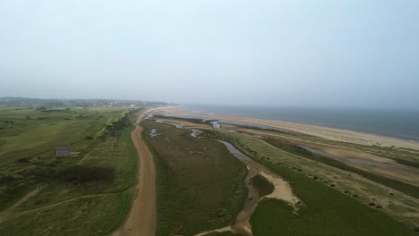 Aerial-shot-of-marsh-land,-sand-dunes-and-sea-in-nature-reserve-in-Norfolk,-England-with-Beach-hut-in-view-and-Hunstanton-in-the-distance