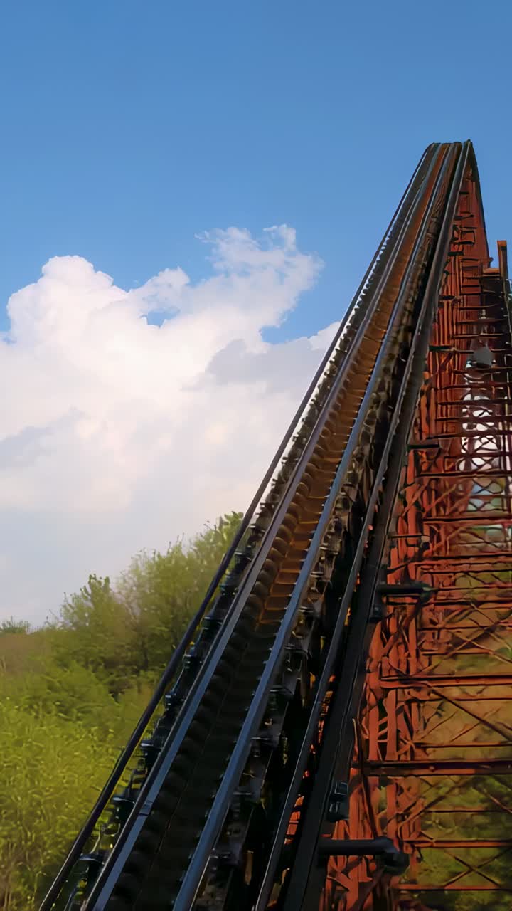 Vertical video: Moving camera filming coaster twin rails rising to hill crest, showing rust trestle