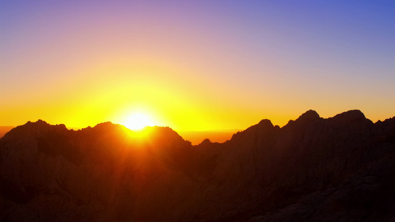 Goldener Sonnenaufgang erhebt sich über dunklen Bergsilhouetten.