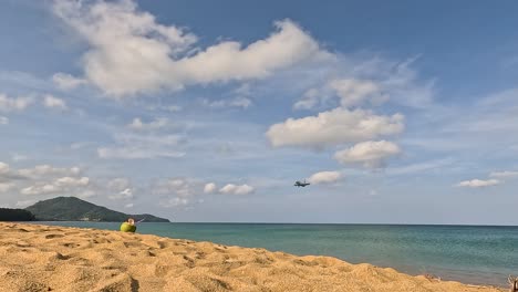 a plane approaches and lands over a sunny beach in phuket, thailand, with clear skies and a serene ocean backdrop