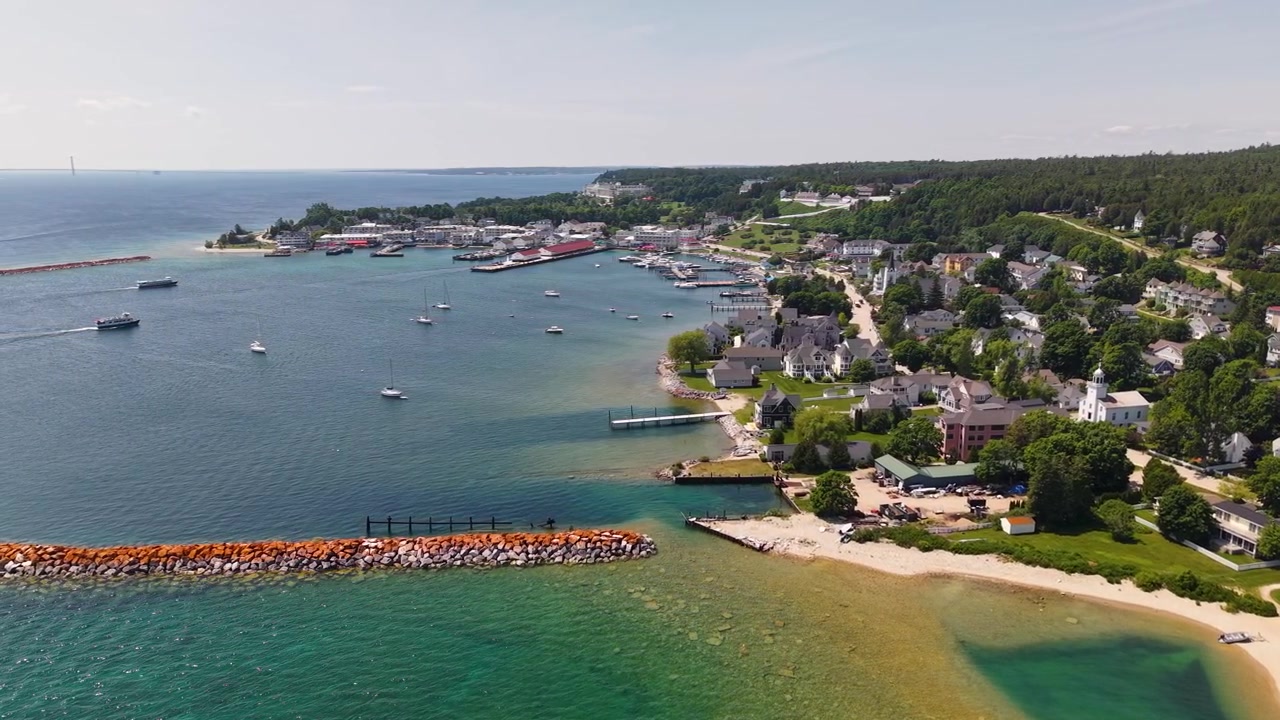 Vista aerea panoramica delle case fronte mare, delle barche nel porto, della spiaggia sabbiosa e del frangiflutti in pietra sull'isola di Mackinac, nel Michigan.