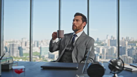 calm professional sipping coffee in panoramic office. pensive businessman rest