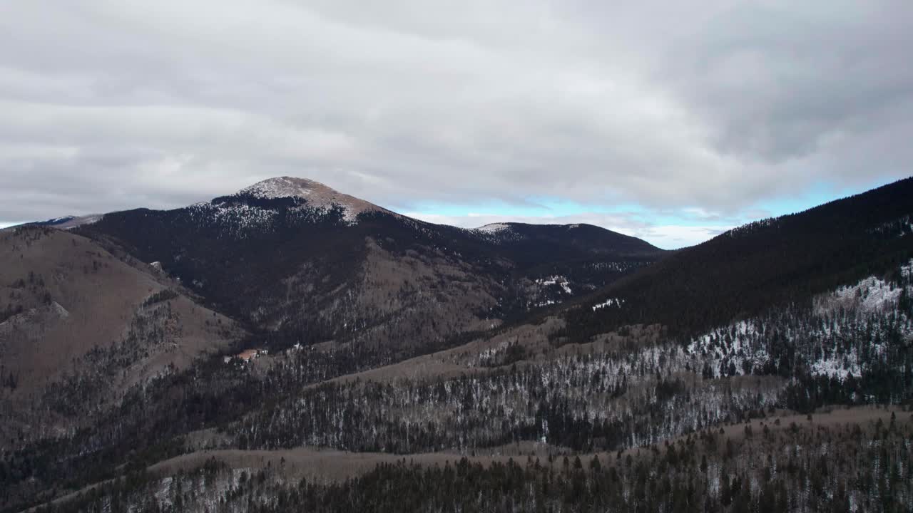toma panorámica de drones de un pico de montaña nevado con nubes y cielos azules